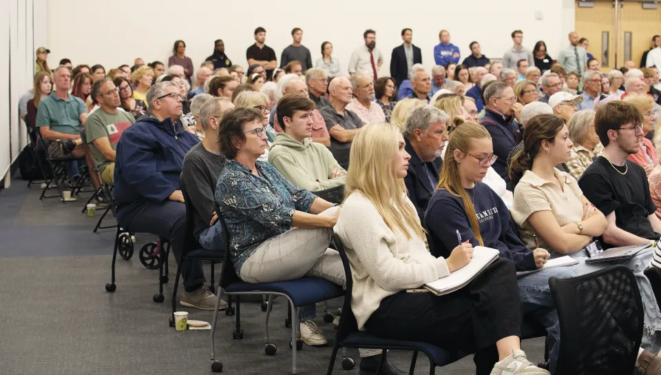 A large audience of community members, students, and faculty fills rows of chairs at the President's Forum.