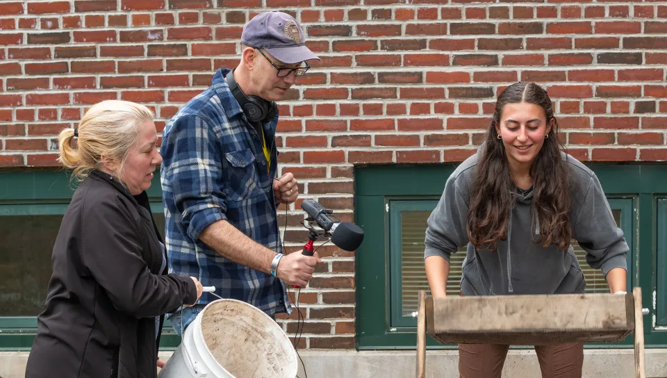 A student holds a wooden screen while Arthur Anderson document the archaeological screening process using video equipment at The Wayside excavation site.