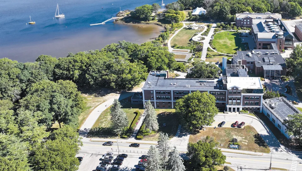 Aerial view of the University of New England's Biddeford Campus showing waterfront academic buildings, sailboats in the harbor, and the site where The Wayside once stood.
