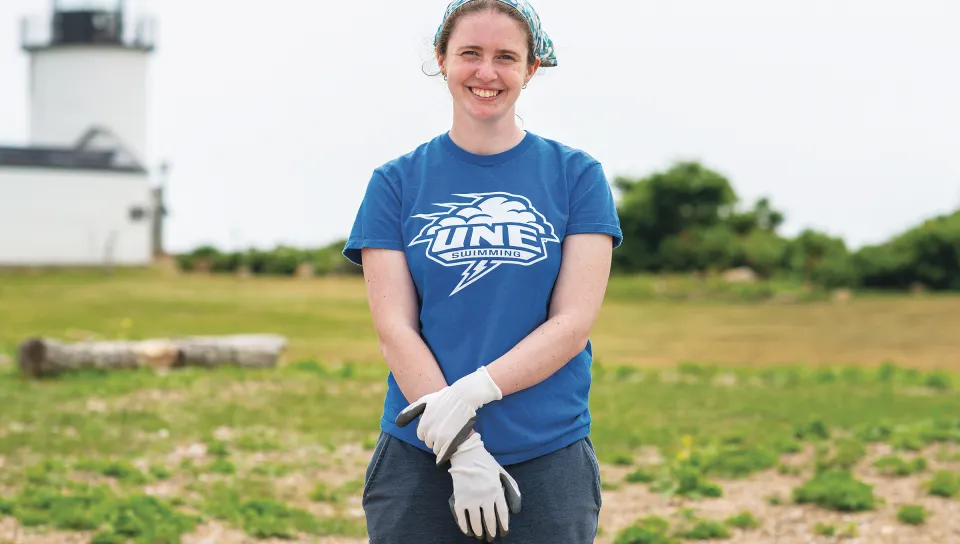 Annika Doeppers poses at Goat Island Light Station wearing a UNE Swimming shirt after completing conservation work.