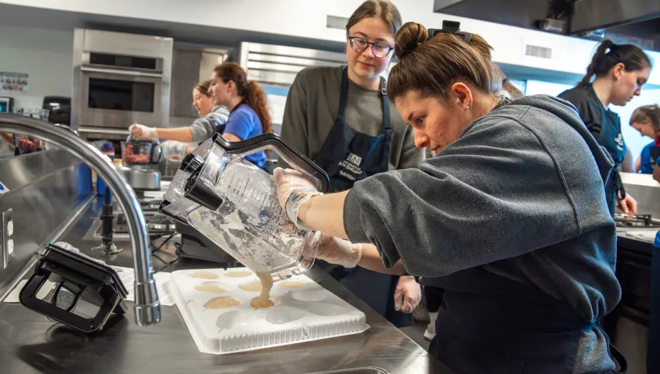 A student group pours a mixture of blended pears into pear-shaped molds to mimic the texture of whole fruit