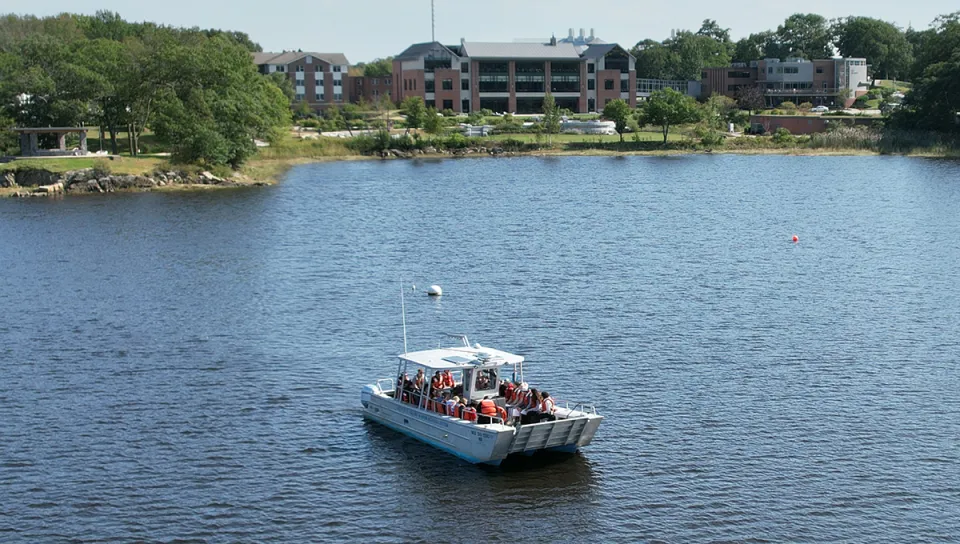 Research boat on calm water with campus buildings in background.