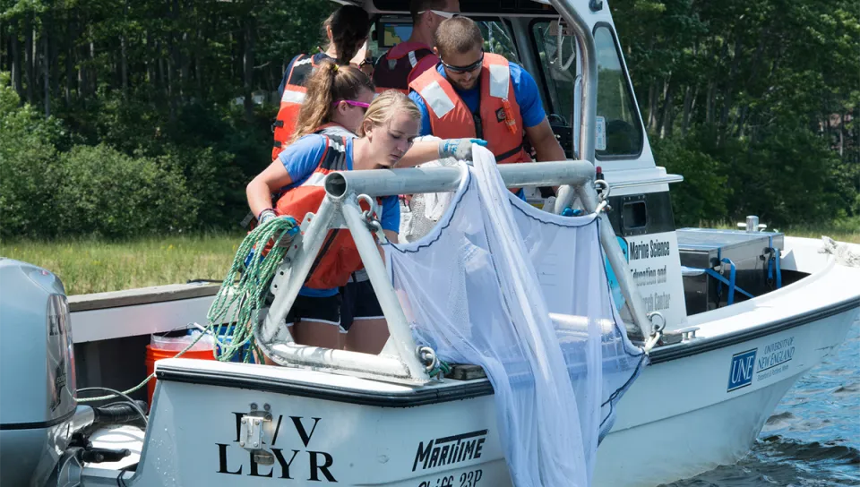 Students in life vests deploy a net from a research boat.