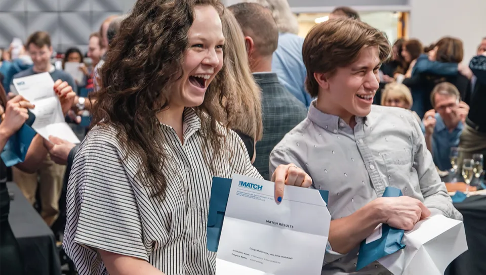 Two U N E College of Osteopathic Medicine students laugh with excitement as they open their Match Day results letters.