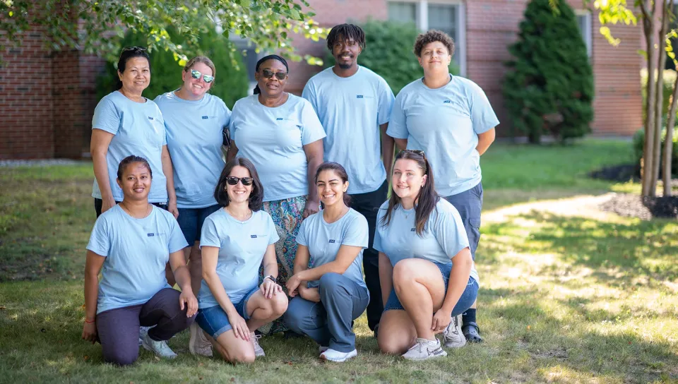A group of U N E employees in matching light blue T-shirts pose together outdoors at the 2026 Fall Assembly.