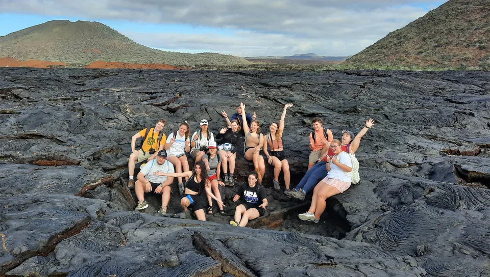 A group of U N E study abroad students pose together on a volcanic lava field in the Galápagos Islands.