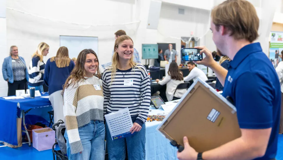 A student intern takes photos on an iPhone of two event attendees