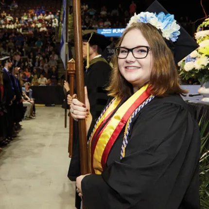 A U N E student stands in front of the crowd holding a flag at commencement