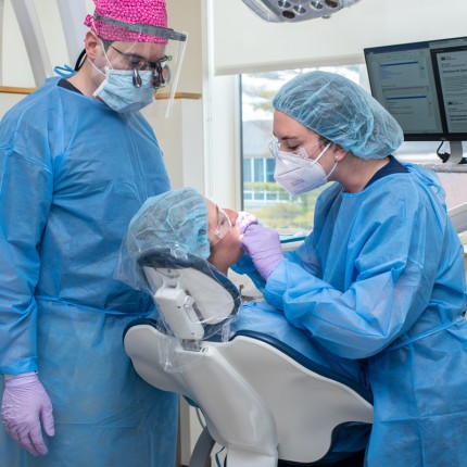 A dental student and a physician assistant student look into the mouth of a patient during a dental screening
