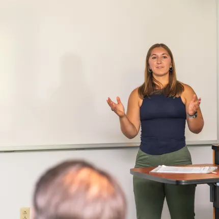 A UNE student speaks to a crowd in a classroom