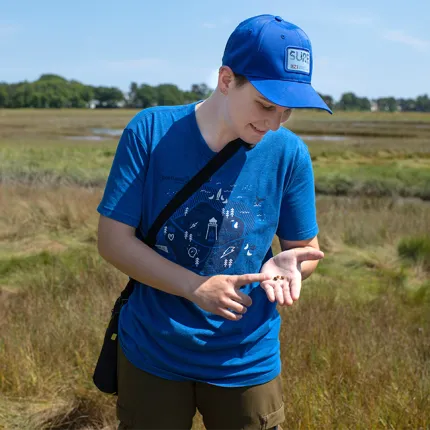 Robyn Rollo holds out a snail on her hand while in the marshes next to the Biddeford Campus