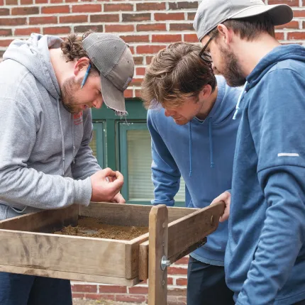 Three UNE students process dirt over the dig site