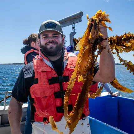 Student in life vest holding up long strands of seaweed