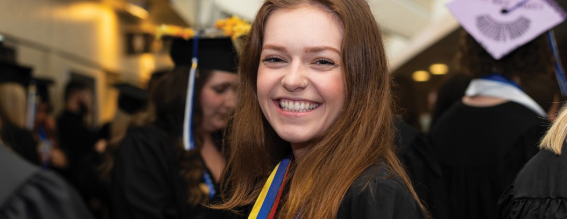 A student stands in the crowd and smiles at the camera after graduation