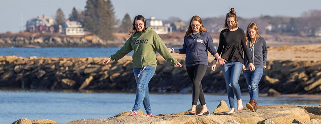 Four students walking on the rocks along the ocean