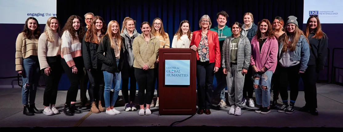 A large group of students stand on stage with a C G H lecturer