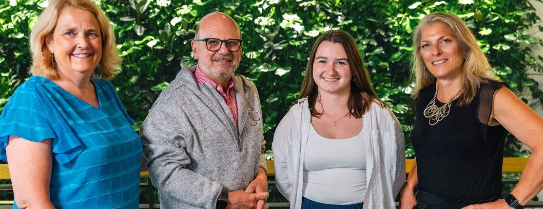 A group of four individuals stand in front of a living green wall