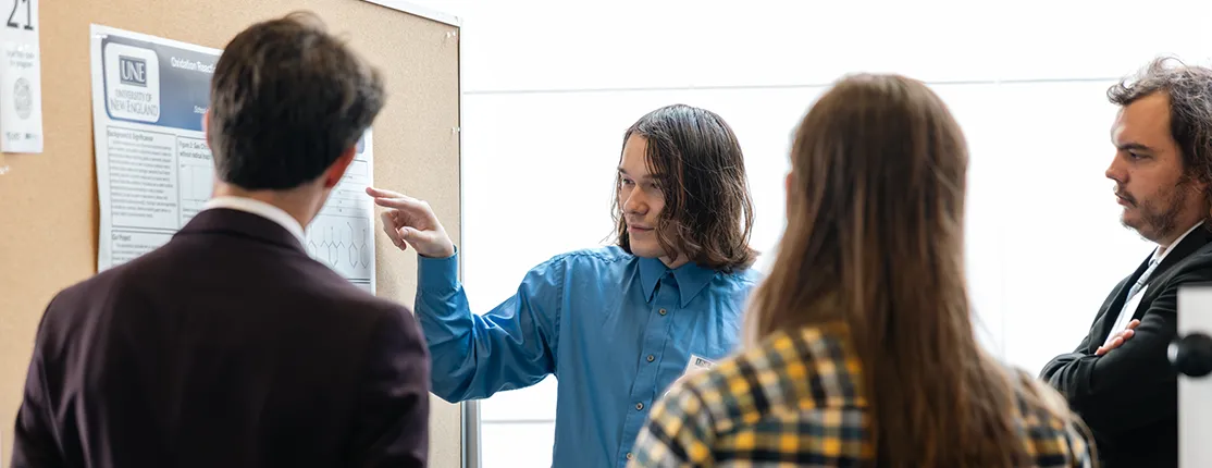 A U N E student presents on their research to a group of interested bystanders at the SURE Fall Research Symposium