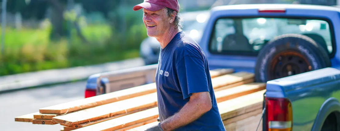 Cameron Wake, Ph.D. while in a red cap and blue shirt unloads lumber from a pickup truck.