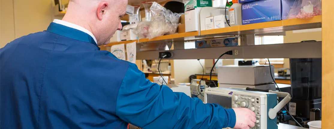 A professor turns a knob on an oscilloscope in a laboratory setting