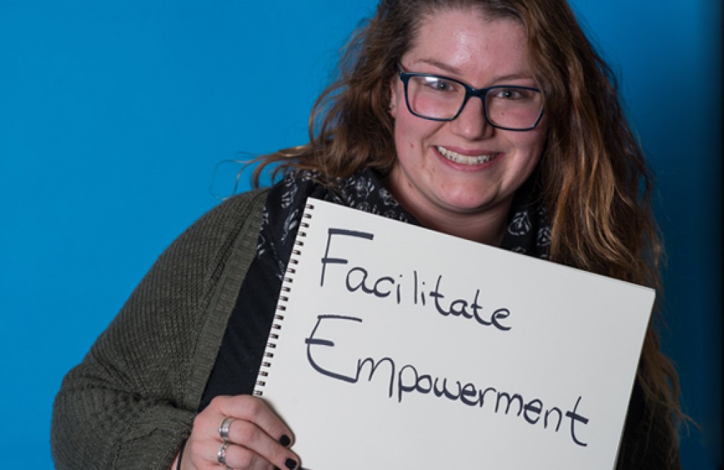 a u n e social work student poses with a handwritten sign reading facilitate empowerment