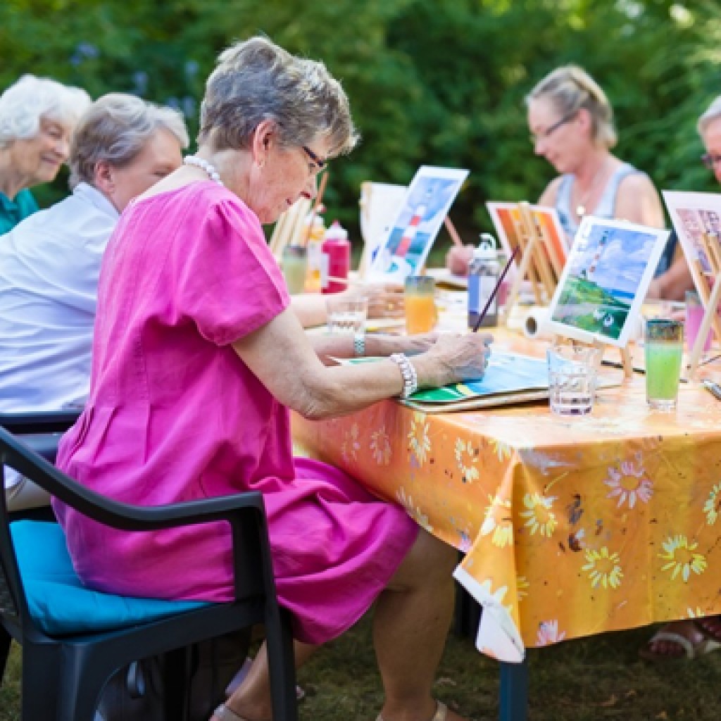 elderly women sit at an outdoor table painting