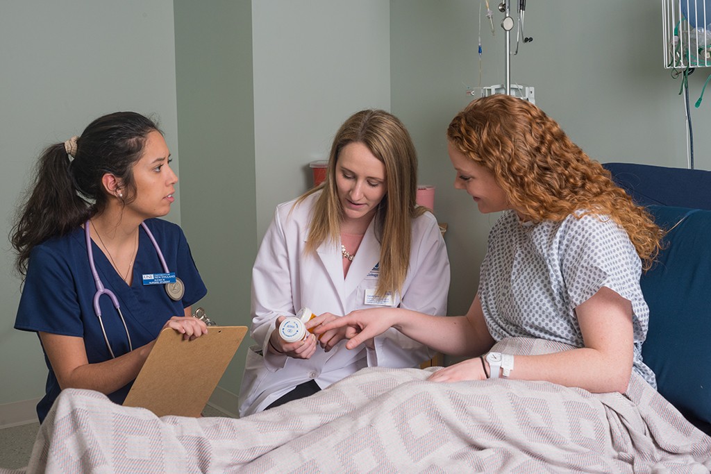 Two U N E health professions students work with a patient in a hospital bed