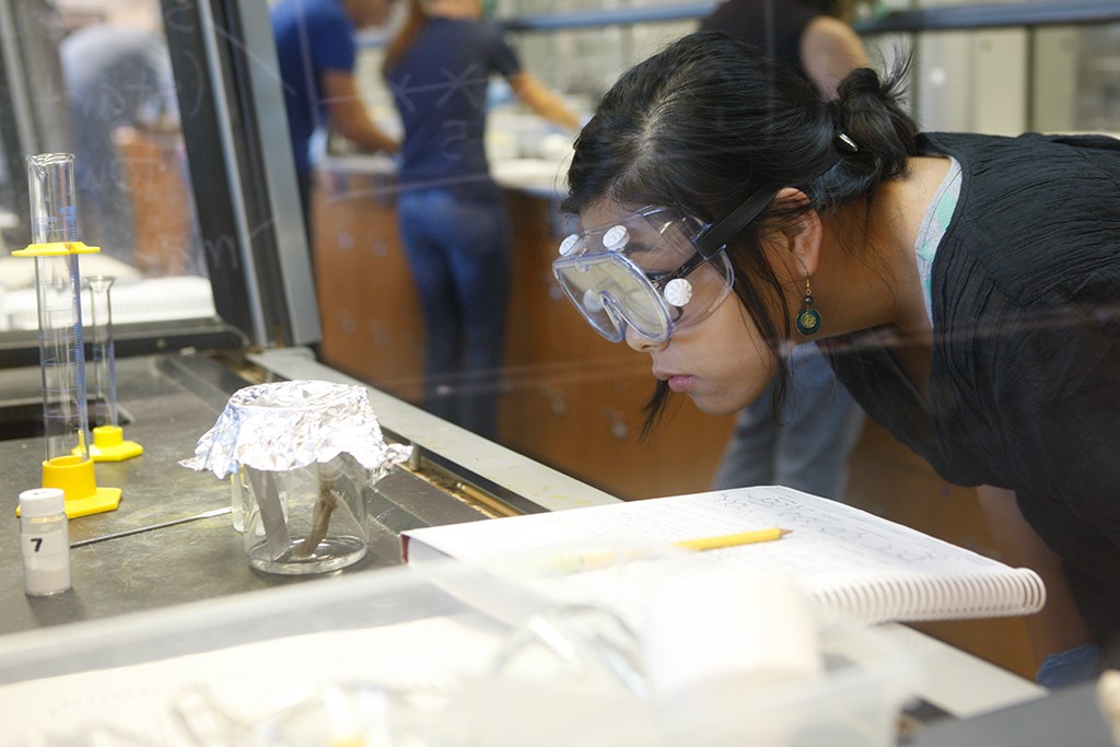 A U N E student wearing safety googles in a lab examines a specimen jar