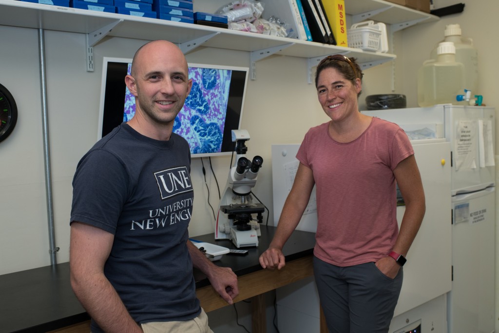 Professors Adam St. Gelais and Carrie Byron stand next to a microscope