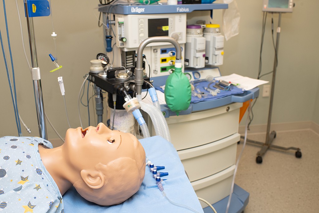 a patient simulator lies on a bed in a clinical simulation room