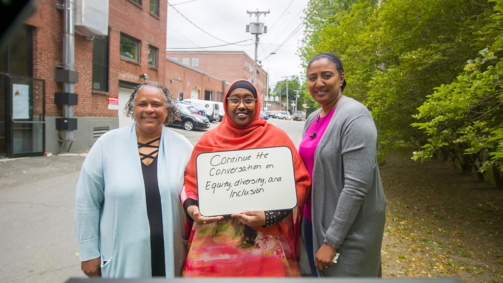 Three U N E employees hold a sign that reads Continue the Conversation on Equity, Diversity, and Inclusion