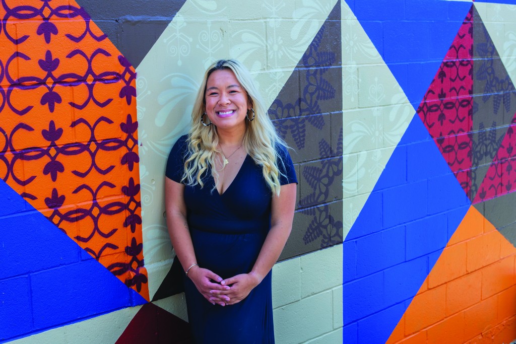 U N E student and professional staff memeber Belle Bocal poses outside in front of a mural painted by Ryan Adams