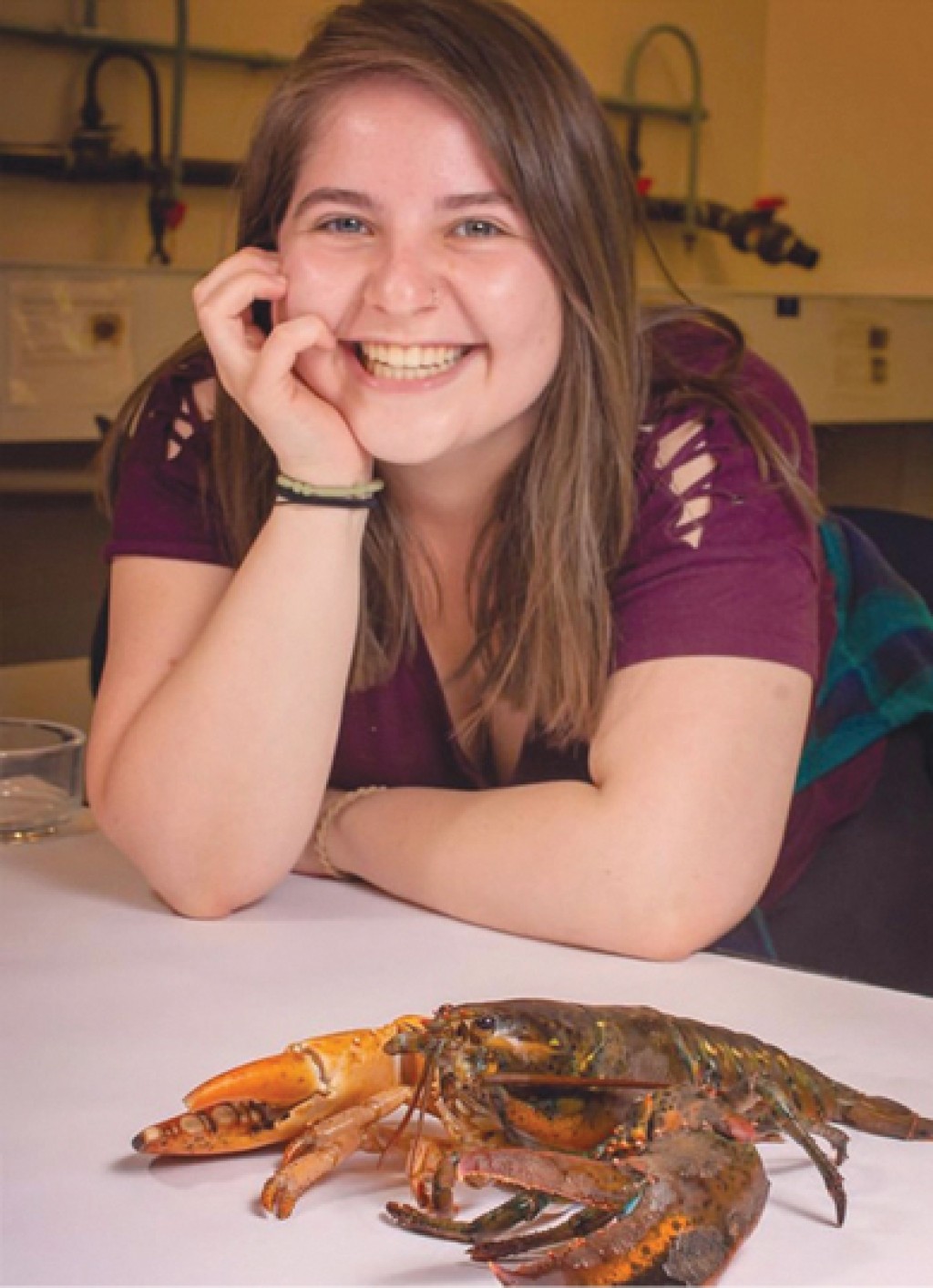 A U N E student smiles while sitting next to a lobster