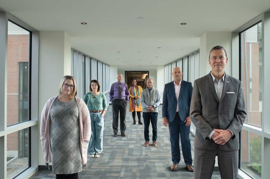 U N E faculty, a student, and President Herbert stand in a hallway
