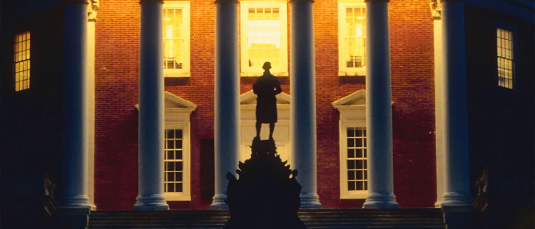 Photo of a statue silhouetted against a college building