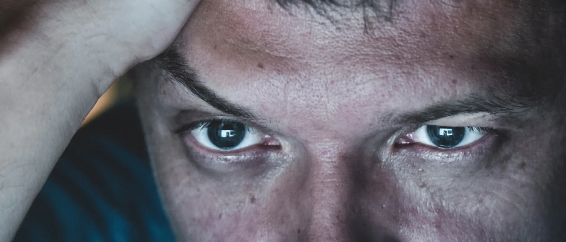 Image of man's eyes illuminated by computer screen, with pained expression.