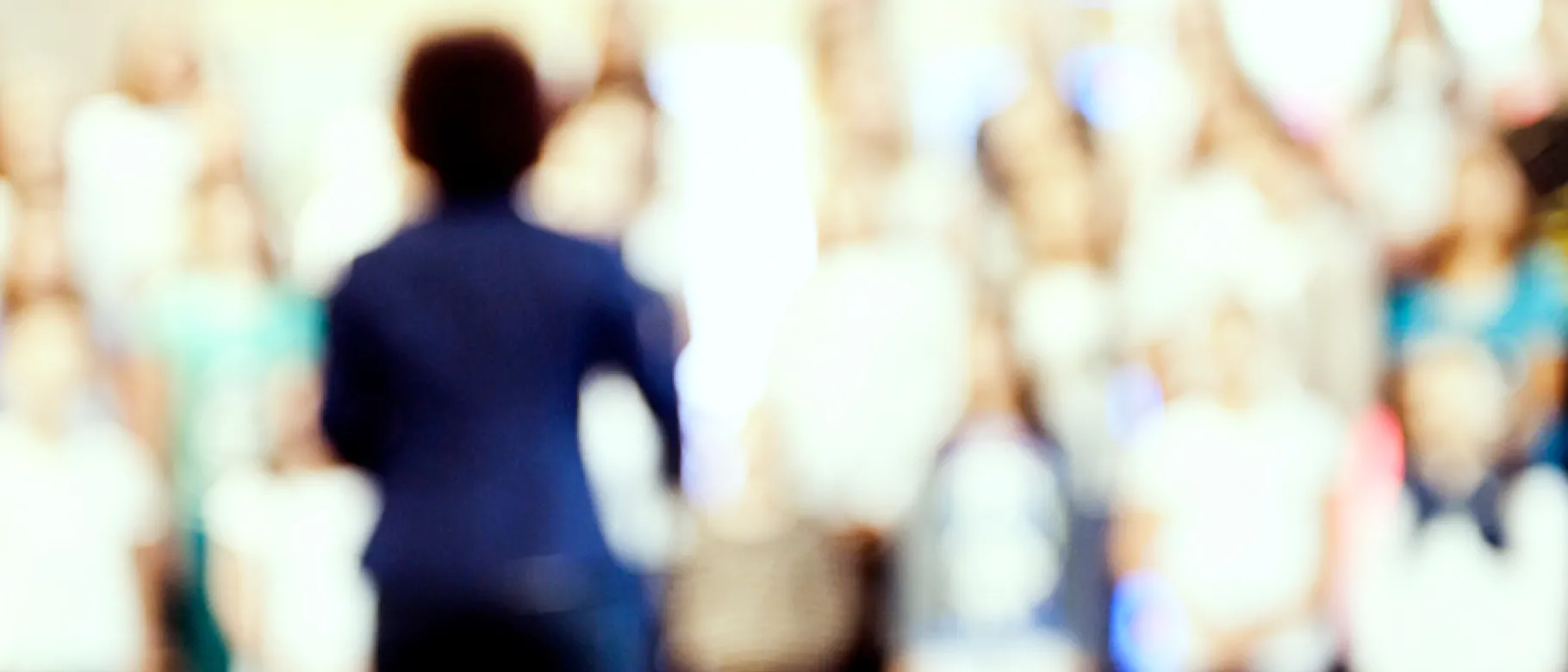 Blurred image of woman with back to camera facing large crowd