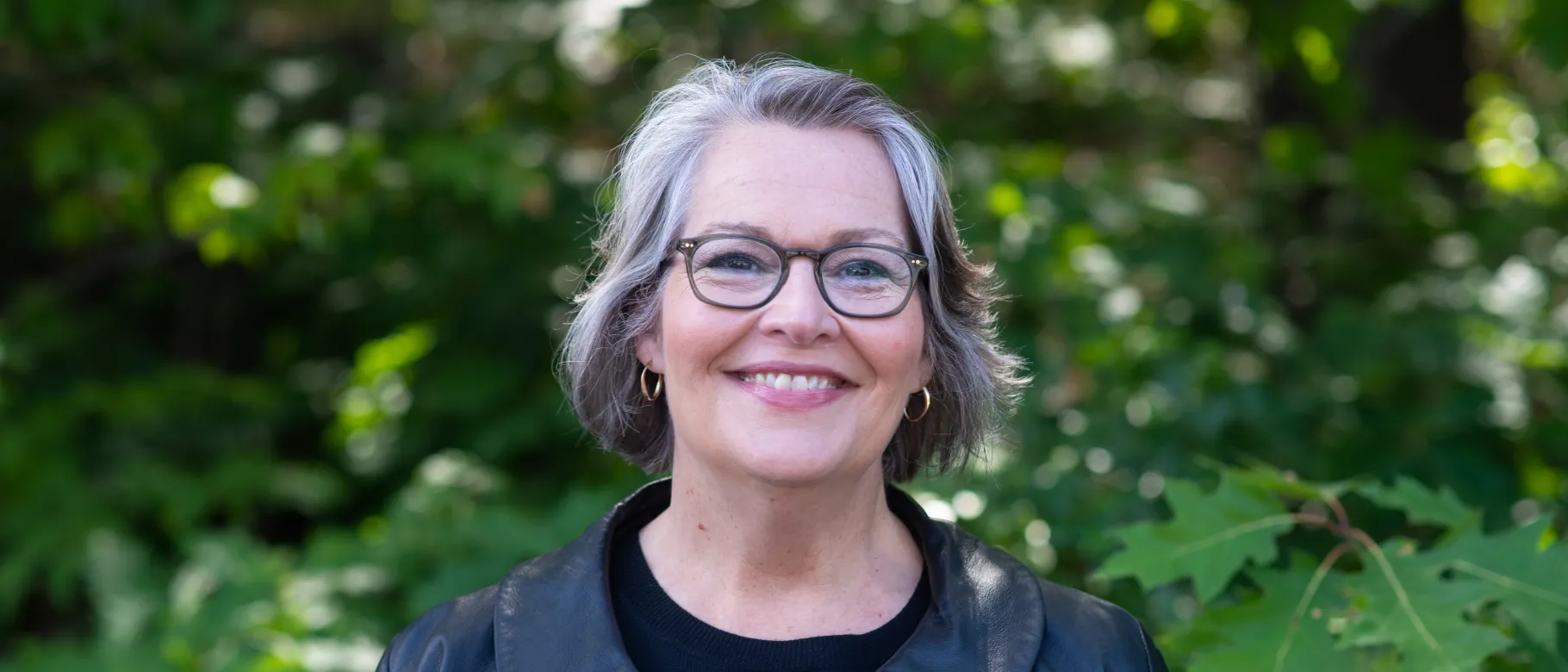 Portrait of Karen Houseknecht smiling against trees