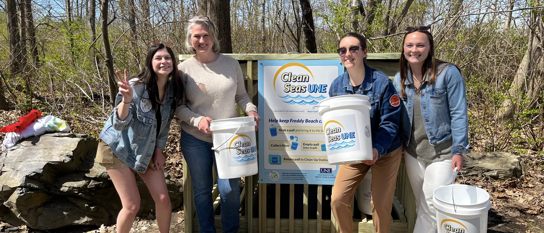 Students and a UNE staff member gather in front of the Clean Seas UNE beach cleanup kiosk at Freddy Beach