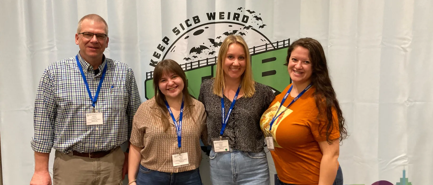 Markus Frederich poses with three students in front of a conference sign