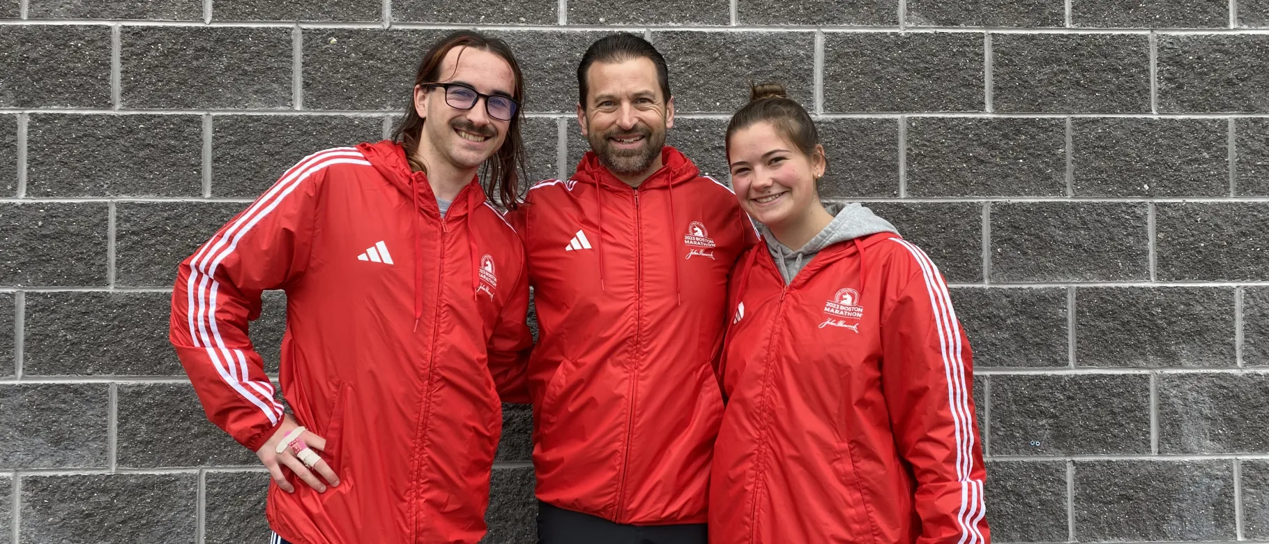Aidan O'Keefe, Christopher Rizzo, and Riley Billings pose in front of a wall at the Boston Marathon