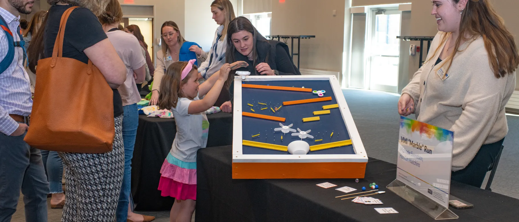 Students instruct a child how tp play with the marble run they built by hand