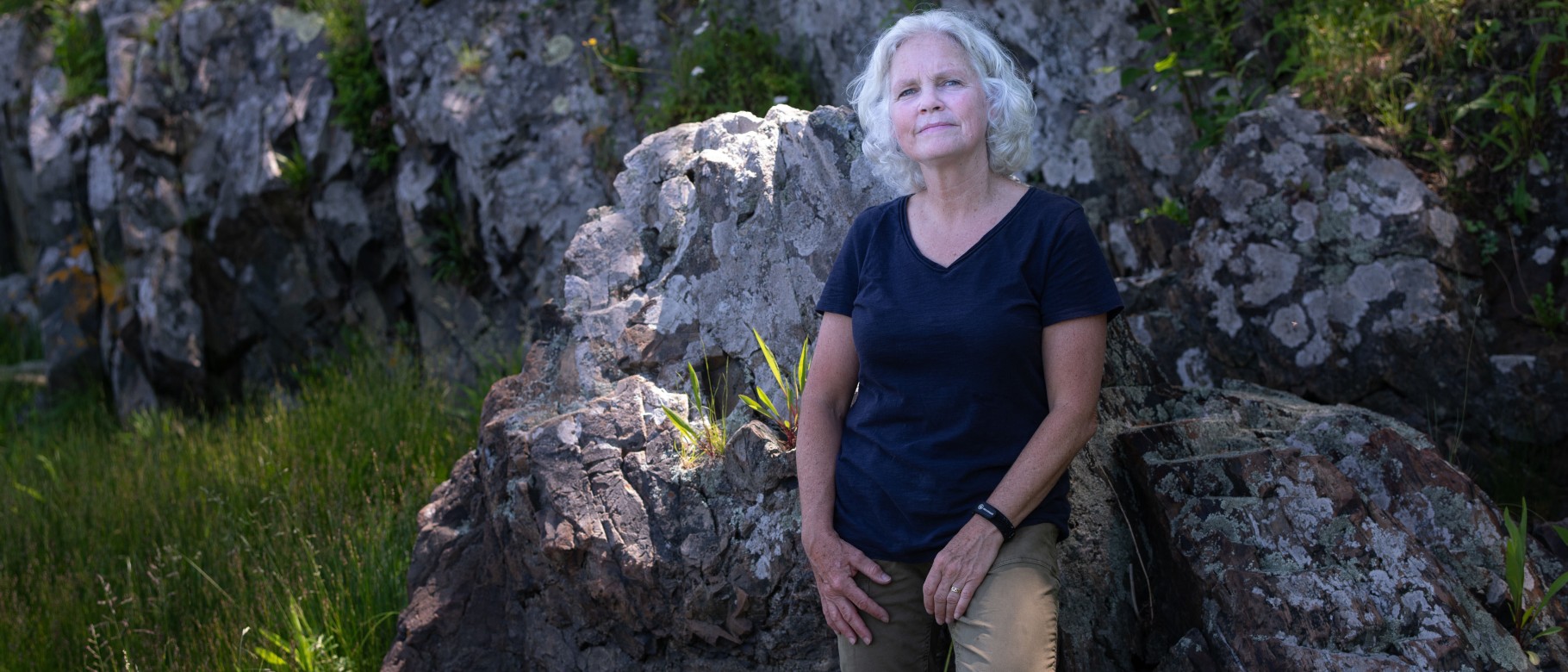 Portrait of Pam Morgan leaning up against a boulder in the woods