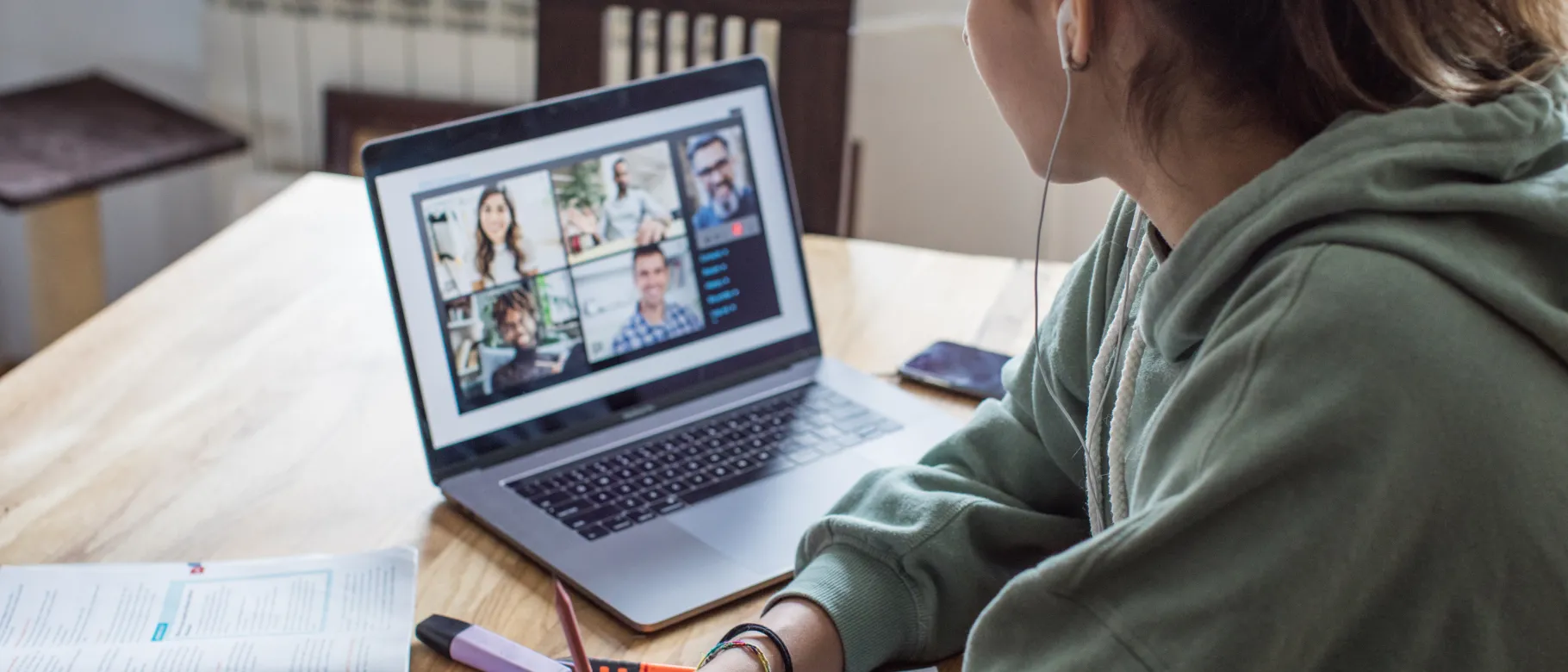 A young woman studying over a video call at a kitchen table