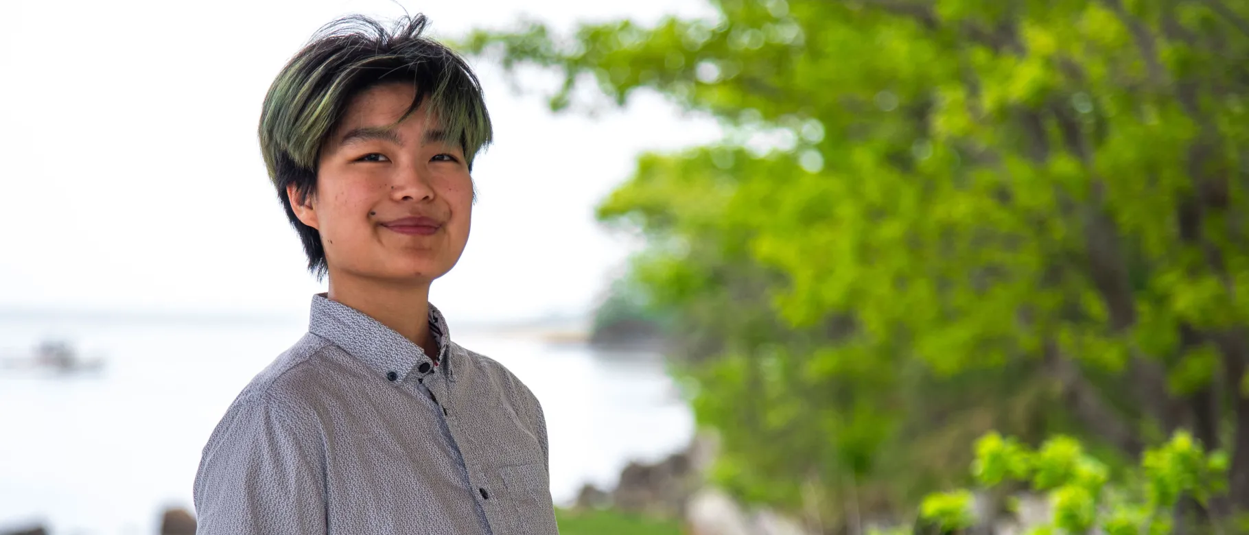 A UNE student poses in front of the Saco River on UNE's campus