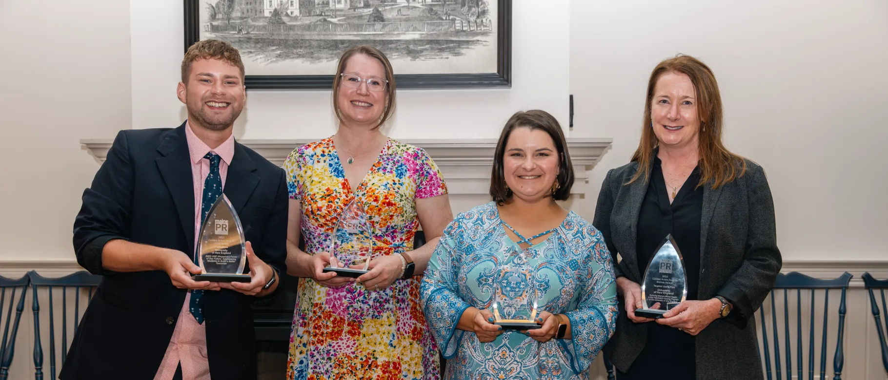 Four members of the Office of Communications pose for a photo in Alumni Hall holding awards