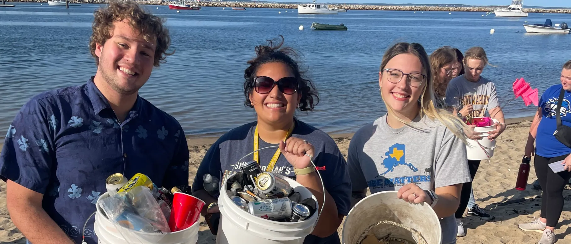 Three UNE students hold buckets of waste after cleaning up Freddy Beach