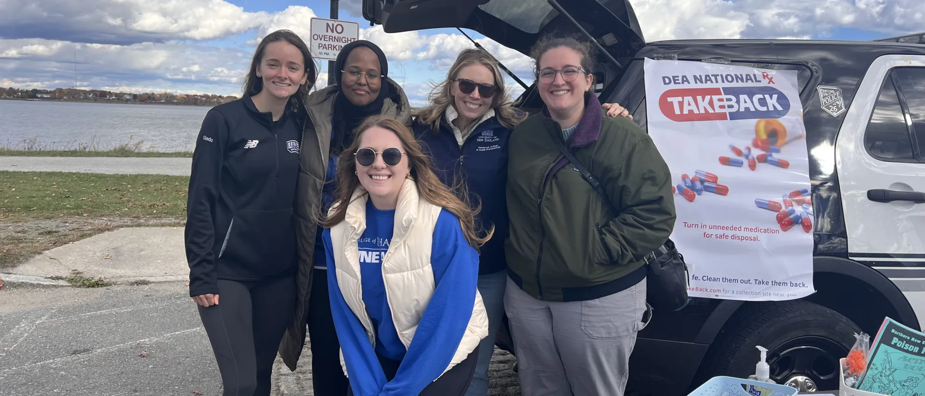 UNE Pharmacy students and faculty pose for a photo by the water at Drug Take Back Day