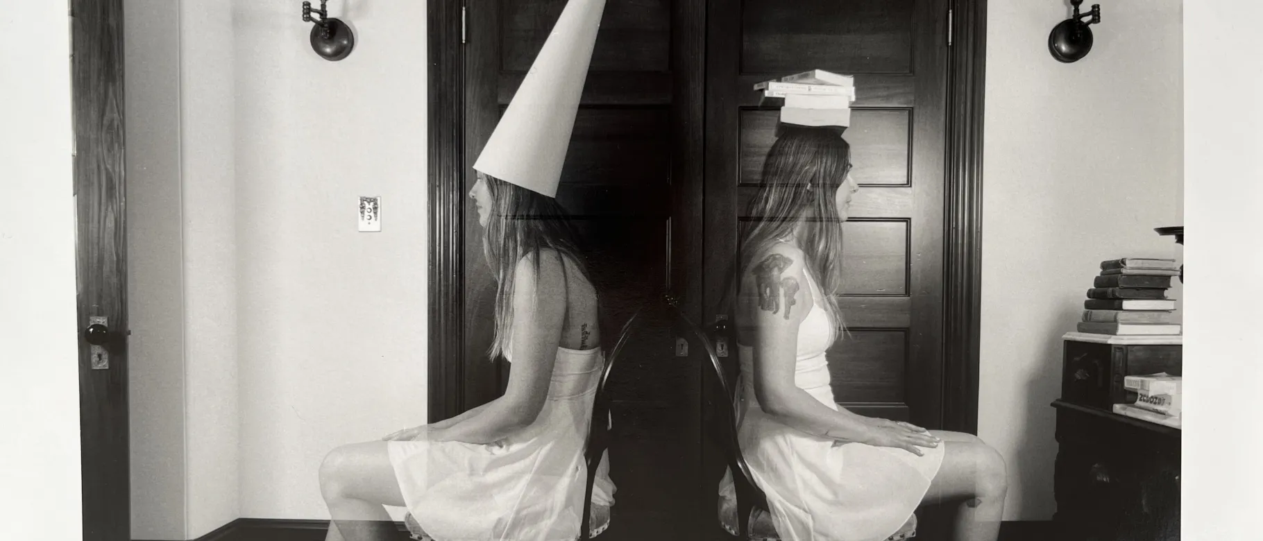 A black and white piece of art depicts one woman in a house sitting in chairs