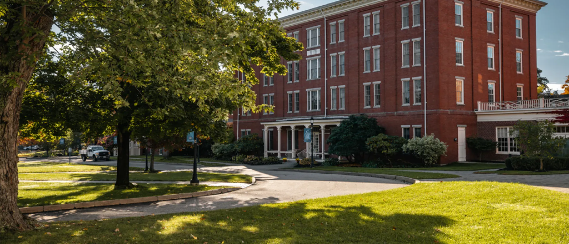 A brick building sits behind green grass and a large tree